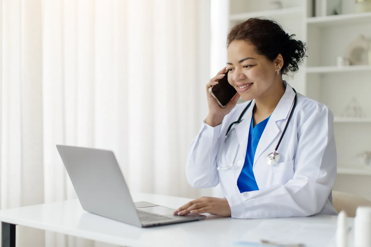 Physician speaking on the phone while using a laptop